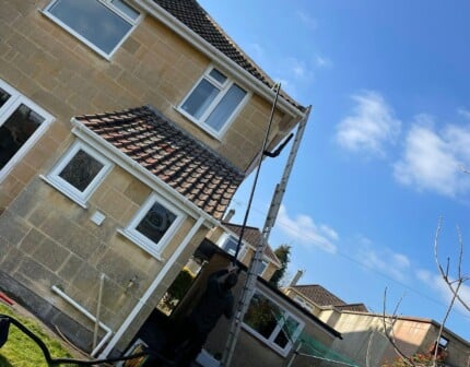Gutter cleaning in Bath and surrounding Somerset areas – worker inserting hose into blocked gutter to clear debris and restore water flow
